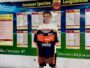 Young boy holding an orange and navy soccer jersey in front of a wall of league schedules and charts.