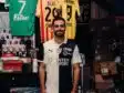 Man in a black-and-white football jersey standing in a team shop with jerseys hanging behind him.