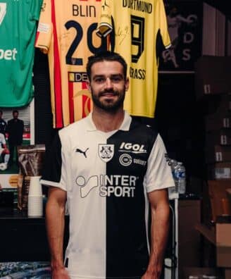 IMG_5121 | AllezPaillade.com Man in a black-and-white football jersey standing in a team shop with jerseys hanging behind him.
