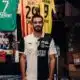 Man in a black-and-white football jersey standing in a team shop with jerseys hanging behind him.