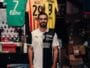 Man in a black-and-white football jersey standing in a team shop with jerseys hanging behind him.