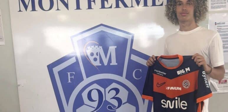 Young man with curly hair posing beside a large Football Club Montfermeil sign, holding a navy and orange Montfermeil football jersey.
