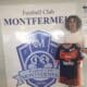 Young man with curly hair posing beside a large Football Club Montfermeil sign, holding a navy and orange Montfermeil football jersey.