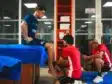 Man in blue shirt sits on a table while two therapists in red shirts treat his foot in a clinic setting.