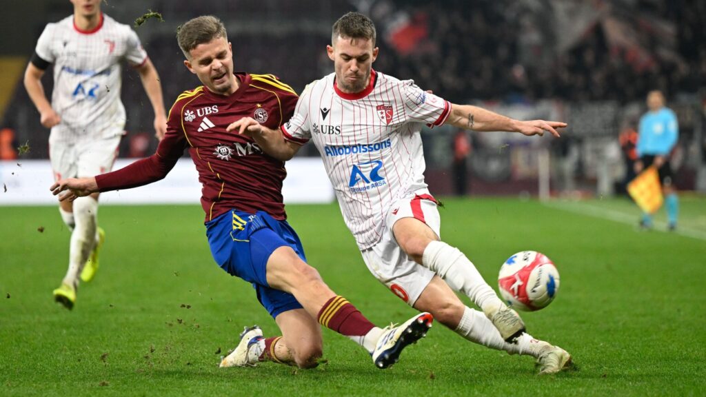 allix servette | AllezPaillade.com Two soccer players in a white-striped kit and a maroon kit challenge for the ball on a green pitch during a match.