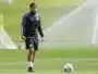 Male soccer player in black training gear standing on a sunny green field with a ball at his feet