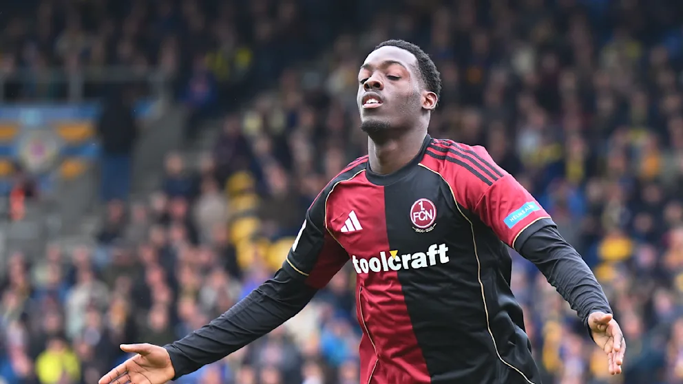 Soccer player in a red-and-black FCN kit celebrating with arms outstretched on a packed stadium field