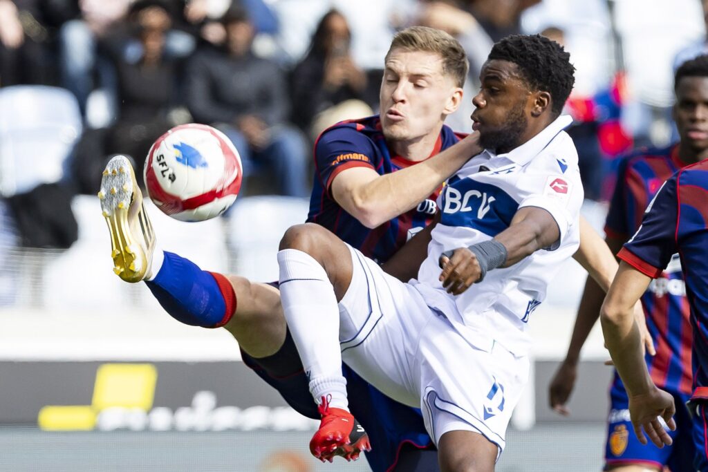 LAUSANNE - BASEL | AllezPaillade.com Two soccer players in white and blue vs navy and red battle for the ball in midair during a match.