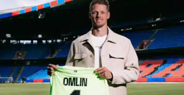 omlin bâle | AllezPaillade.com Football player on a stadium field holding a neon green jersey that reads 'OMLIN' and number 1, smiling at camera.