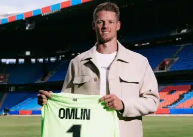 Football player on a stadium field holding a neon green jersey that reads 'OMLIN' and number 1, smiling at camera.