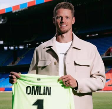 Football player on a stadium field holding a neon green jersey that reads 'OMLIN' and number 1, smiling at camera.