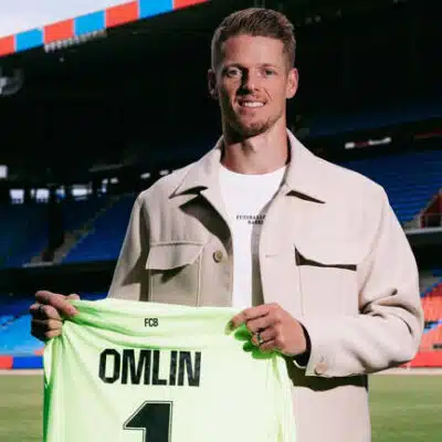 Football player on a stadium field holding a neon green jersey that reads 'OMLIN' and number 1, smiling at camera.