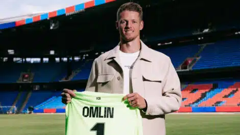 Football player on a stadium field holding a neon green jersey that reads 'OMLIN' and number 1, smiling at camera.