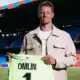 Football player on a stadium field holding a neon green jersey that reads 'OMLIN' and number 1, smiling at camera.