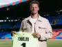 Football player on a stadium field holding a neon green jersey that reads 'OMLIN' and number 1, smiling at camera.