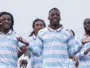 Five male athletes in light blue and white striped jerseys pose together and smile on a sports field, signaling victory.