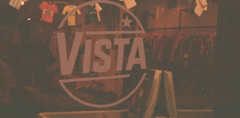 Design sans titre 8 | AllezPaillade.com Interior of a clothing store with a large VISTA logo and circular emblem, shirts on racks in the background and a front display shelf in the foreground.