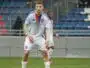 Soccer player in a Lyon jersey standing on a green field with a stadium background, ready to play.