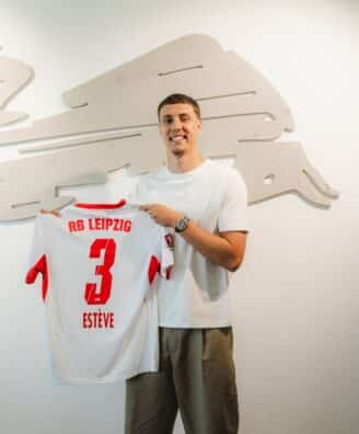 HNaqj5eXIAAryFu | AllezPaillade.com Man in a white T-shirt smiles while holding a white RB Leipzig jersey with the number 3, in front of a pale wall sculpture.