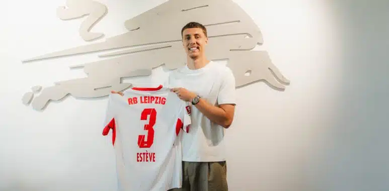 HNaqj5eXIAAryFu | AllezPaillade.com Man in a white T-shirt smiles while holding a white RB Leipzig jersey with the number 3, in front of a pale wall sculpture.