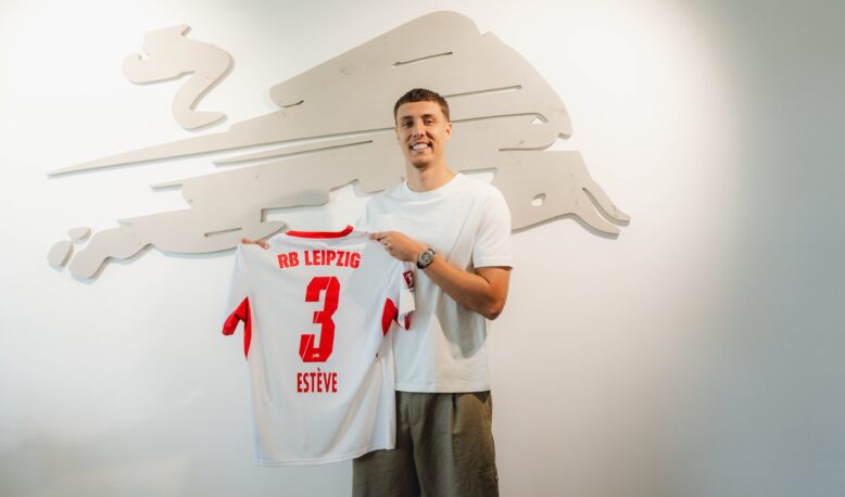 HNaqj5eXIAAryFu | AllezPaillade.com Man in a white T-shirt smiles while holding a white RB Leipzig jersey with the number 3, in front of a pale wall sculpture.