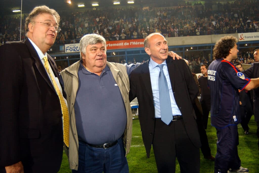 Georges Freche Louis Nicollin Gerard Collomb | AllezPaillade.com Three men in suits standing on a field, arms around each other, crowd watching a sports event in the stands behind them.