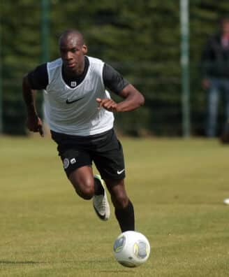 Soccer player in a white training vest dribbles the ball on a grassy field, teammates blurred in the background during practice.]','Soccer practice scene with a central player in a white vest chasing the ball on a sunny day.