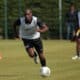 Soccer player in a white training vest dribbles the ball on a grassy field, teammates blurred in the background during practice.]','Soccer practice scene with a central player in a white vest chasing the ball on a sunny day.