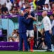 Soccer players shake hands on the sideline during a FIFA World Cup match (Qatar 2022), with a cameraman filming nearby.