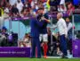 Soccer players shake hands on the sideline during a FIFA World Cup match (Qatar 2022), with a cameraman filming nearby.