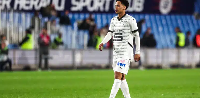 Montpellier HSC v Stade Rennais FC - Ligue 1 McDonalds 20242025 | AllezPaillade.com Soccer player in a white patterned jersey walking on a grass pitch with blurred stadium seating in the background.