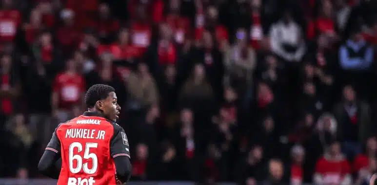 Nordan Mukiele Stade Rennais FC v RC Lens - Ligue 1 McDonalds 20252026 | AllezPaillade.com Soccer player Mukiele Jr. in a red jersey with number 65, seen from behind, on a crowded stadium.