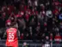 Soccer player Mukiele Jr. in a red jersey with number 65, seen from behind, on a crowded stadium.