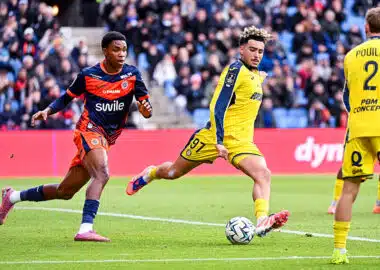 Soccer players in yellow and blue uniforms chase the ball on a green field with a crowd in the stands watching a match ongoing behind them.