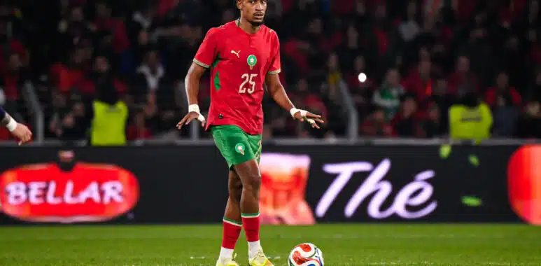 Halhal Morocco v Paraguay - Friendly Match 31032026 | AllezPaillade.com Soccer player in red jersey with green shorts dribbling the ball on a green field during a match with a crowded stadium behind him
