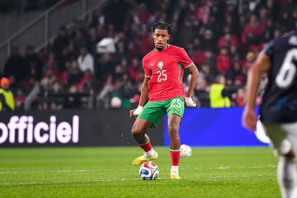 Halhal Morocco v Paraguay - Friendly Match 31032026 | AllezPaillade.com Soccer player in red jersey with number 25 dribbling the ball on a green pitch with a crowd in the stands behind him