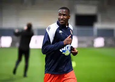 Male soccer player in navy and white jacket running on a green field during training, with blurred background.