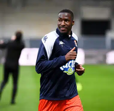Male soccer player in navy and white jacket running on a green field during training, with blurred background.