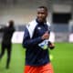 Male soccer player in navy and white jacket running on a green field during training, with blurred background.