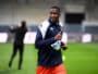 Male soccer player in navy and white jacket running on a green field during training, with blurred background.