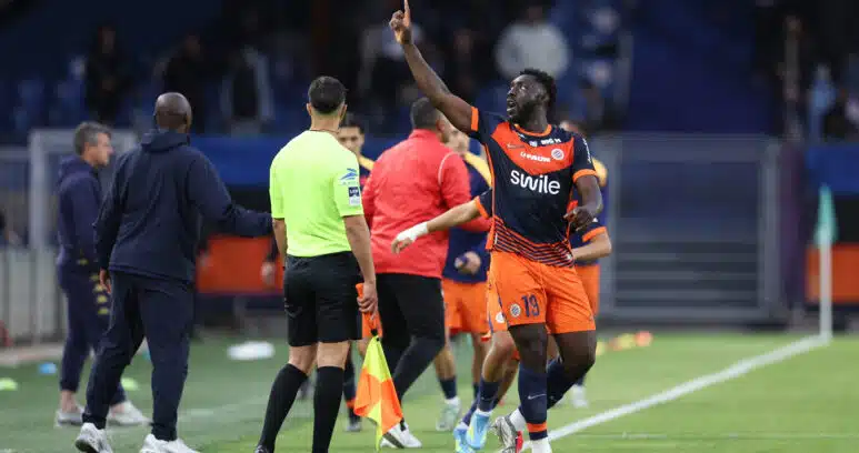 Alexandre Mendy Montpellier Herault SC v Clermont Foot 63 - Ligue 2 BKT 20252026 | AllezPaillade.com Soccer player in orange and navy kit lifts his right index finger while sprinting along the sideline, with teammates and officials nearby on the field.