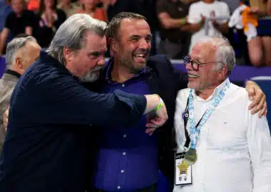 Three men hug in celebration at a sports event, central man smiling as others join in.