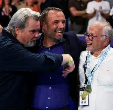 Three men hug in celebration at a sports event, central man smiling as others join in.
