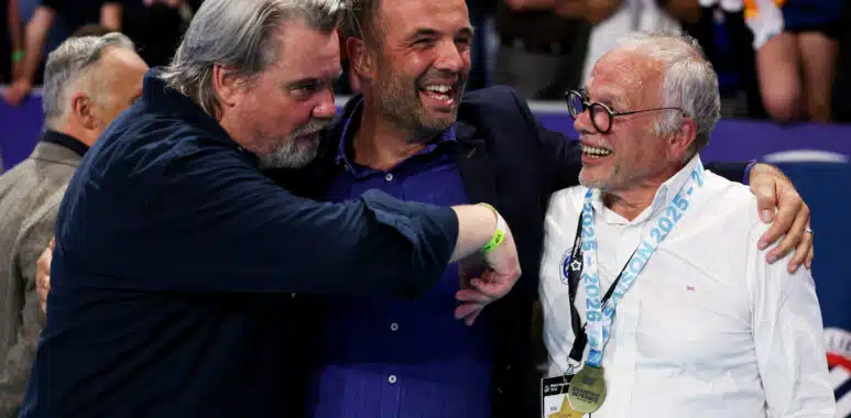 Three men hug in celebration at a sports event, central man smiling as others join in.
