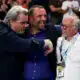Three men hug in celebration at a sports event, central man smiling as others join in.