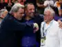 Three men hug in celebration at a sports event, central man smiling as others join in.