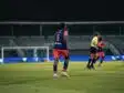 Soccer player wearing blue jersey number 5 stands on a green field during a night match, near teammates and a goalie in the background.
