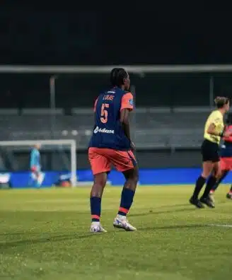Soccer player wearing blue jersey number 5 stands on a green field during a night match, near teammates and a goalie in the background.