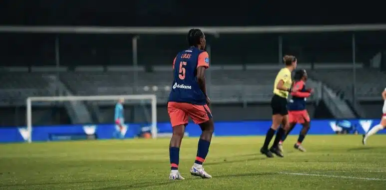 Screenshot | AllezPaillade.com Soccer player wearing blue jersey number 5 stands on a green field during a night match, near teammates and a goalie in the background.