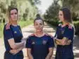 Three women in matching navy blue sports jerseys with orange accents stand on a sunlit, tree-lined path, arms crossed and facing the camera.